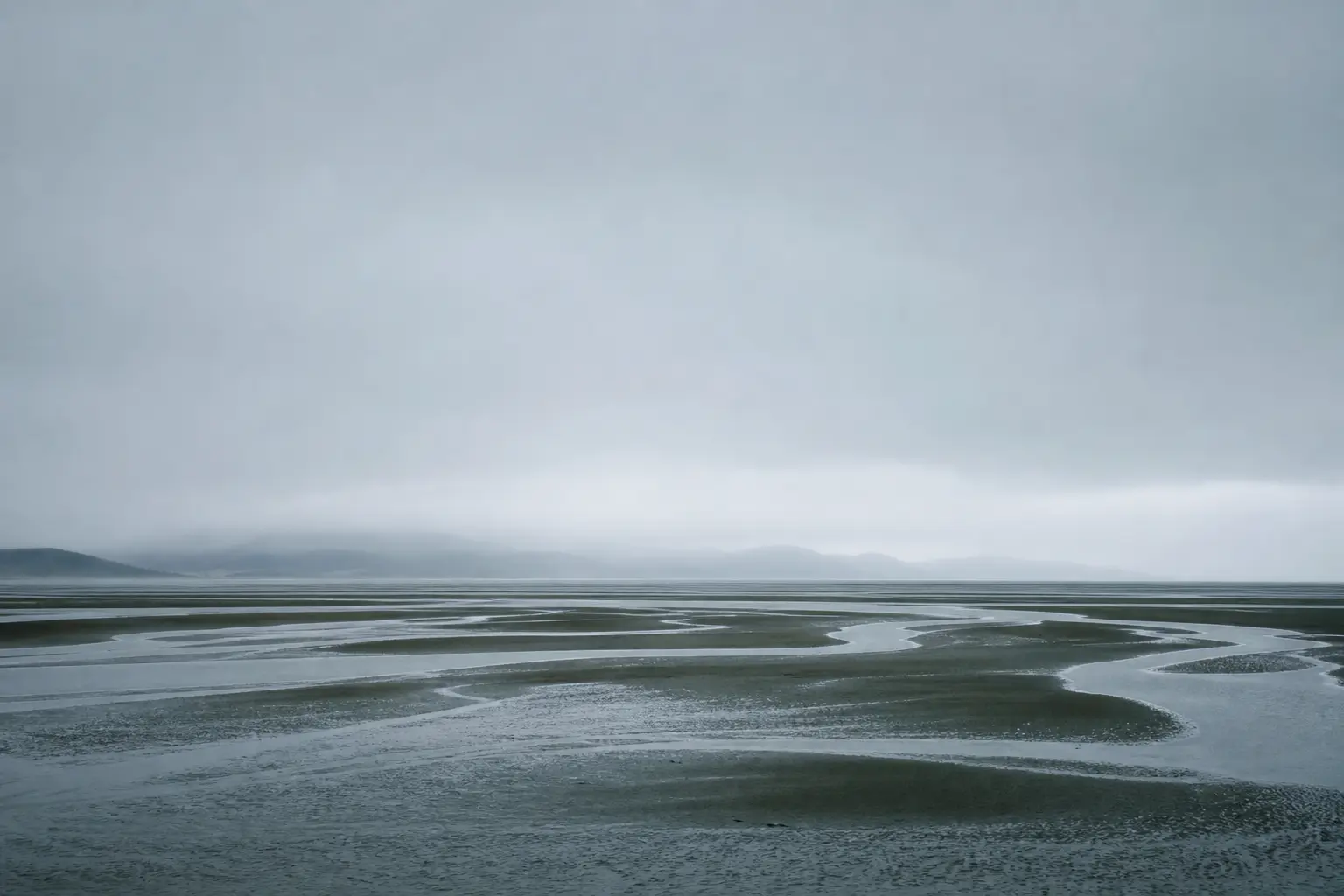 A flat estuary at low tide under an overcast sky